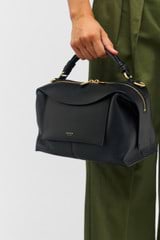 Profile view of model wearing the Oroton Mica Small Bowler in Black and Pebble grain leather with smooth leather trims for Women